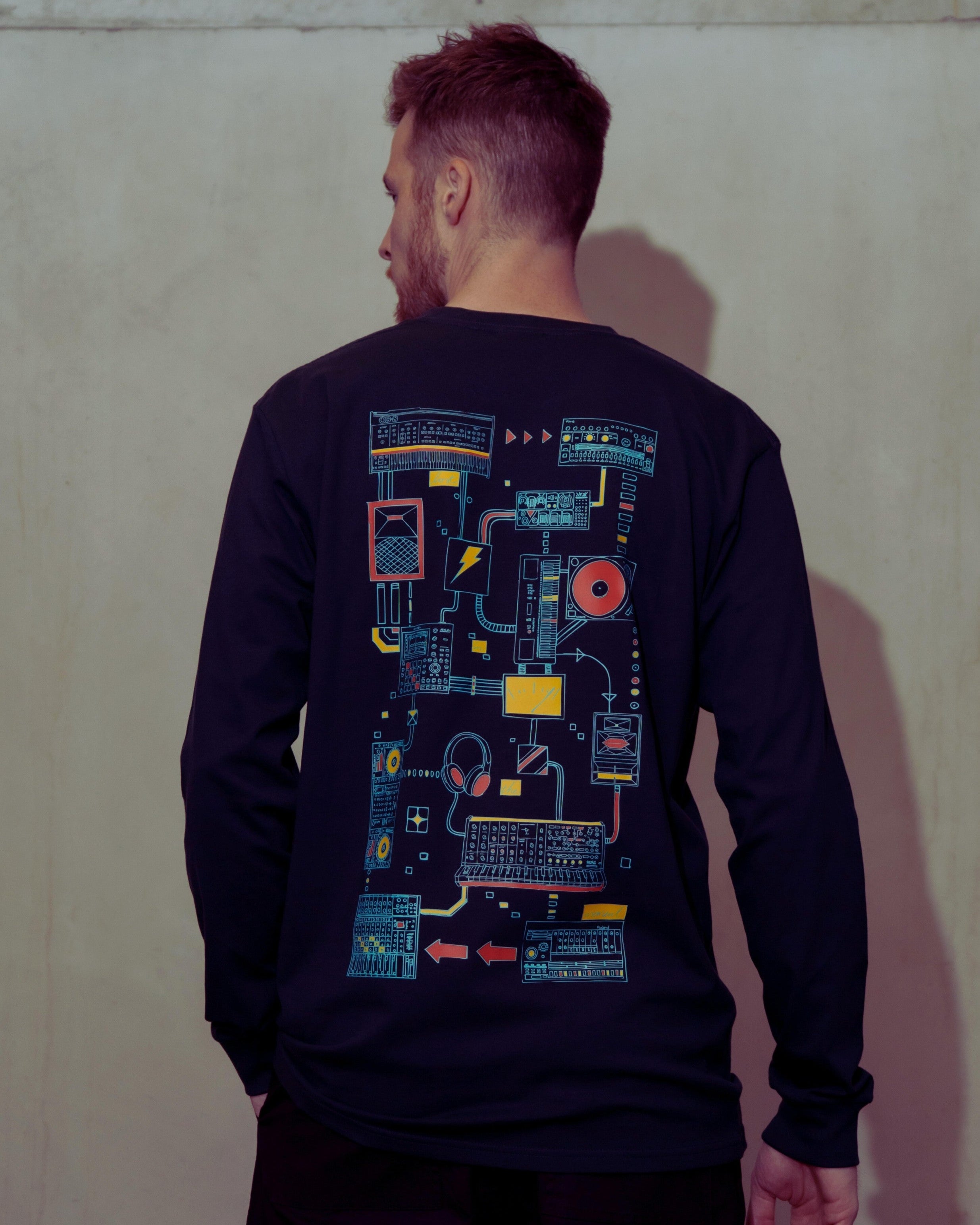 Person wearing a black long-sleeve shirt with colorful circuit-like design on the back against a plain wall.